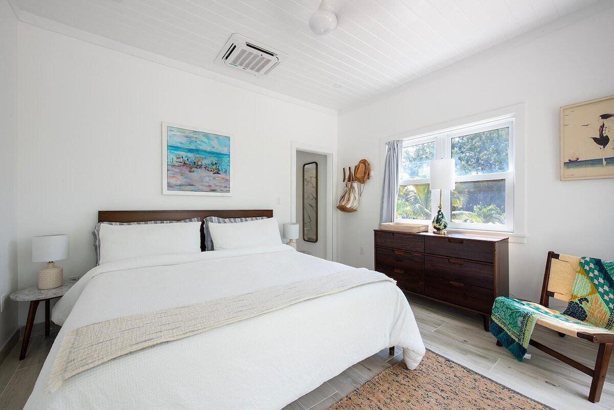 A bedroom with a large bed, a dresser, a chair, and a window with curtains.