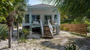 A beach house with a wooden deck, a staircase, and a view of the ocean.