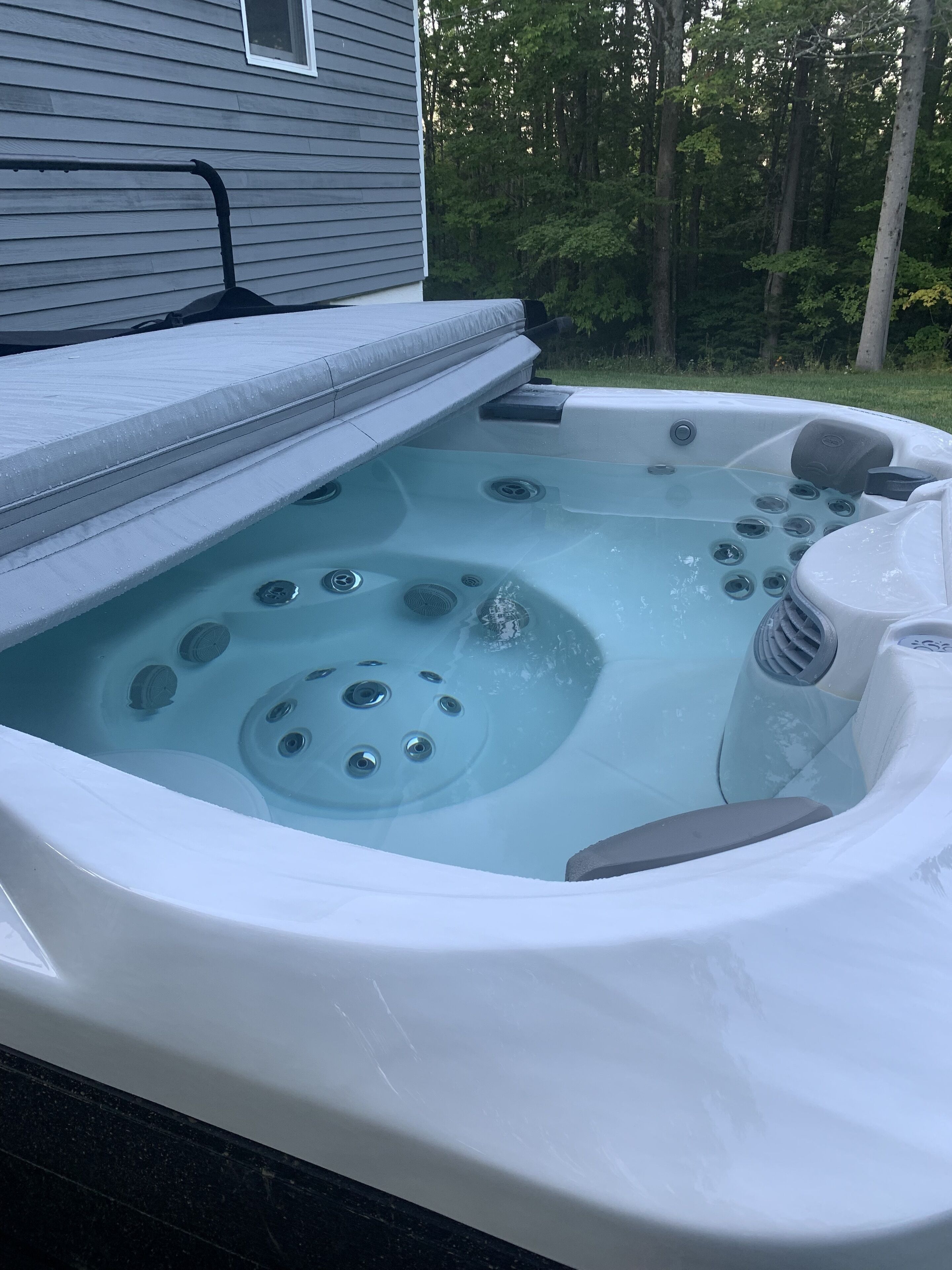 Un bain à remous doté d’un siège intégré et d’un panneau de commande, entouré d’une terrasse en bois et avec une maison en arrière-plan.