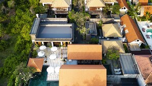 An aerial view of a resort with multiple bungalow-style buildings, a central swimming pool, and lush greenery surrounding the property.