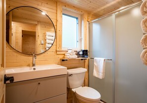 A wooden cabin bathroom with a sink, toilet, and a mirror. - Akira Lodge - Alpha Mountain Lodging + Sauna (Revelstoke)
