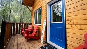 Una baita di legno con una porta blu, un cartello di benvenuto e poltrone Adirondack rosse su un molo di legno.