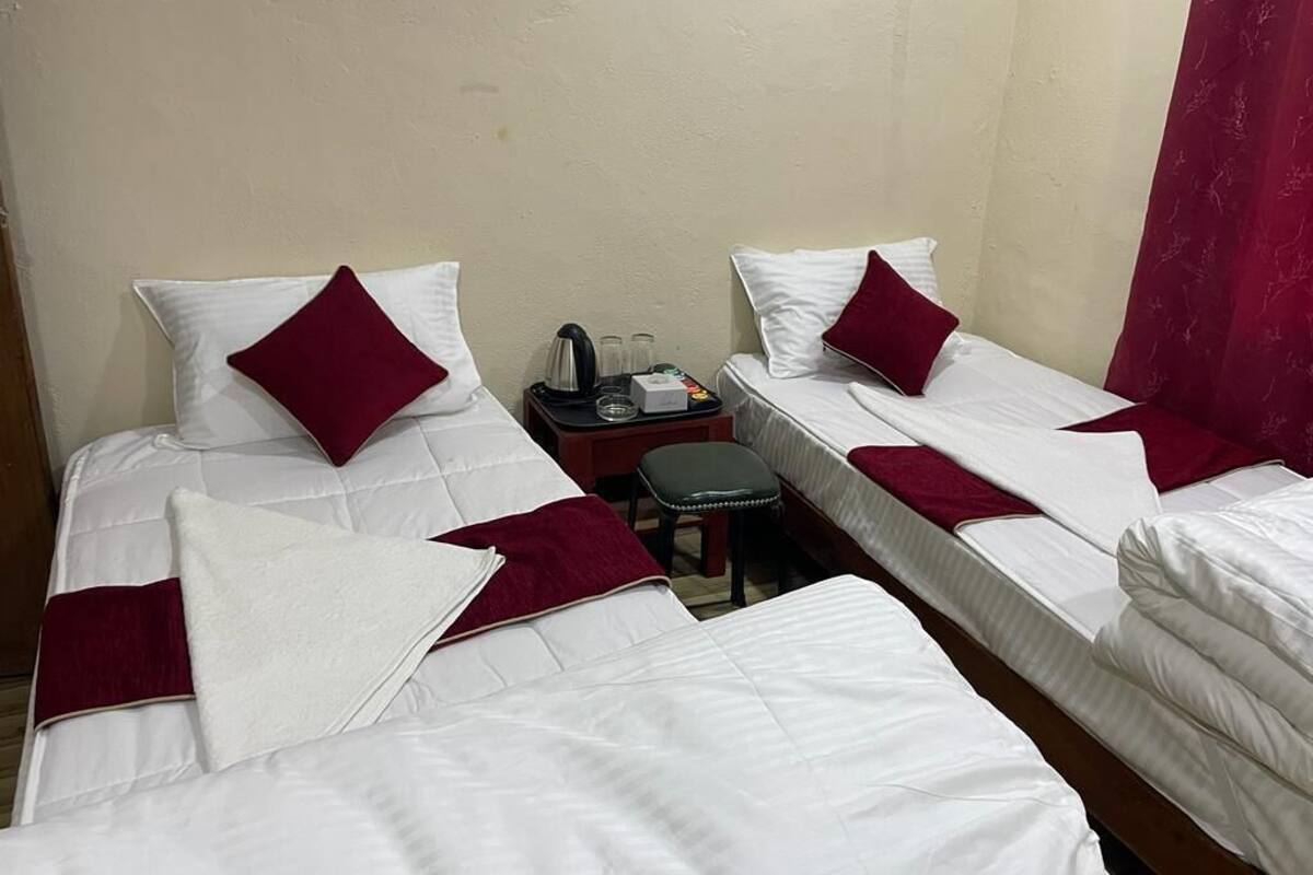 Habitació d'hotel amb dos llits individuals, cadascun amb roba de llit blanca i almoinos vermells. Hi ha una taula petita amb una papereta i tasses, i un tamboret verd.