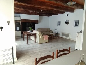 Uma sala de estar com sofá, mesa de jantar e área de cozinha com eletrodomésticos.