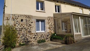 Una casa de dos pisos con fachada de piedra, un porche cubierto y cielo despejado.
