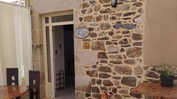 Un patio al aire libre con un muro de piedra, una mesa de madera, sillas y una mecedora.