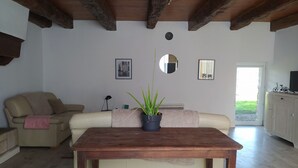 Una sala de estar con una mesa de madera, dos sofás, una planta en maceta, un espejo y una puerta que da al exterior.