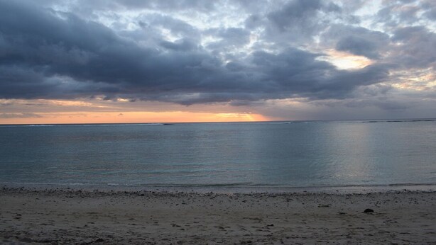A beach with a wide sandy shore and a calm sea under a cloudy sky. - Seafront Apartment Villa (Flic en Flac)