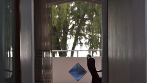 A room with a view of trees through a window, a blue diamond-shaped decoration on the wall, and a chair in the corner. - Seafront Apartment Villa (Flic en Flac)