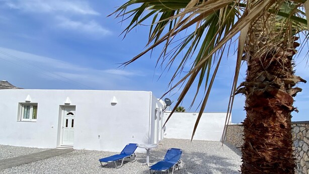 Un edificio blanco con dos sillones azules y una palmera al frente.