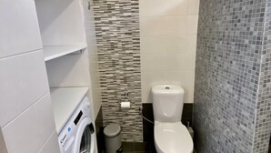Un baño pequeño con lavadora, inodoro y zona de ducha con azulejos.