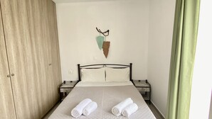 Una cama bien hecha con dos toallas enrolladas, un armario de madera, un adorno en la pared y una cortina verde.