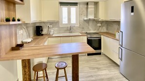 Una cocina moderna con encimera de madera, dos taburetes, un refrigerador de acero inoxidable y una ventana con vistas.