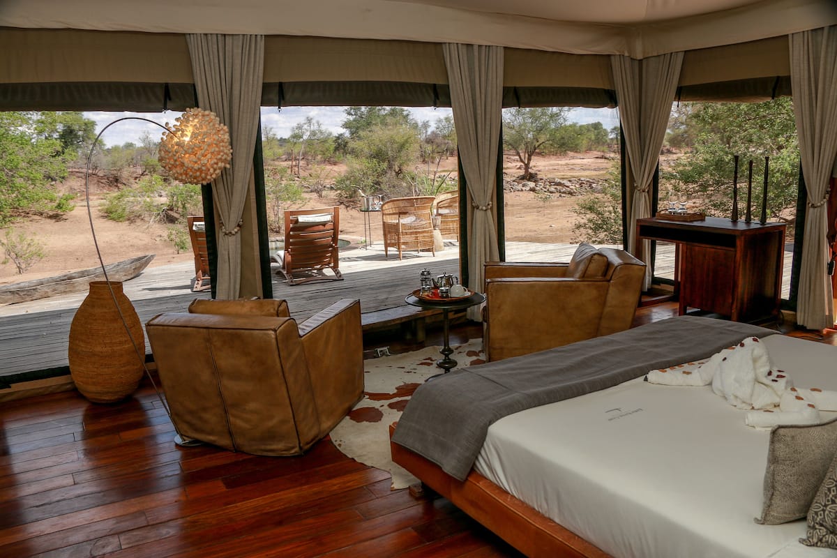 A spacious room with a large bed, two chairs, a small table, and a view of the surrounding landscape.