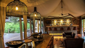 A wooden interior with a bar area, leather seating, and large windows overlooking greenery. - Koro River Camp  (Tuli Lodge)