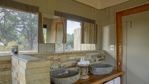 A bathroom with a stone sink, wooden vanity, and a large mirror. - Koro River Camp  (Tuli Lodge)