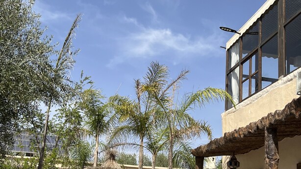 A pool area with lounge chairs, a pergola, and a building with large windows. - Oloft (Marrakech)
