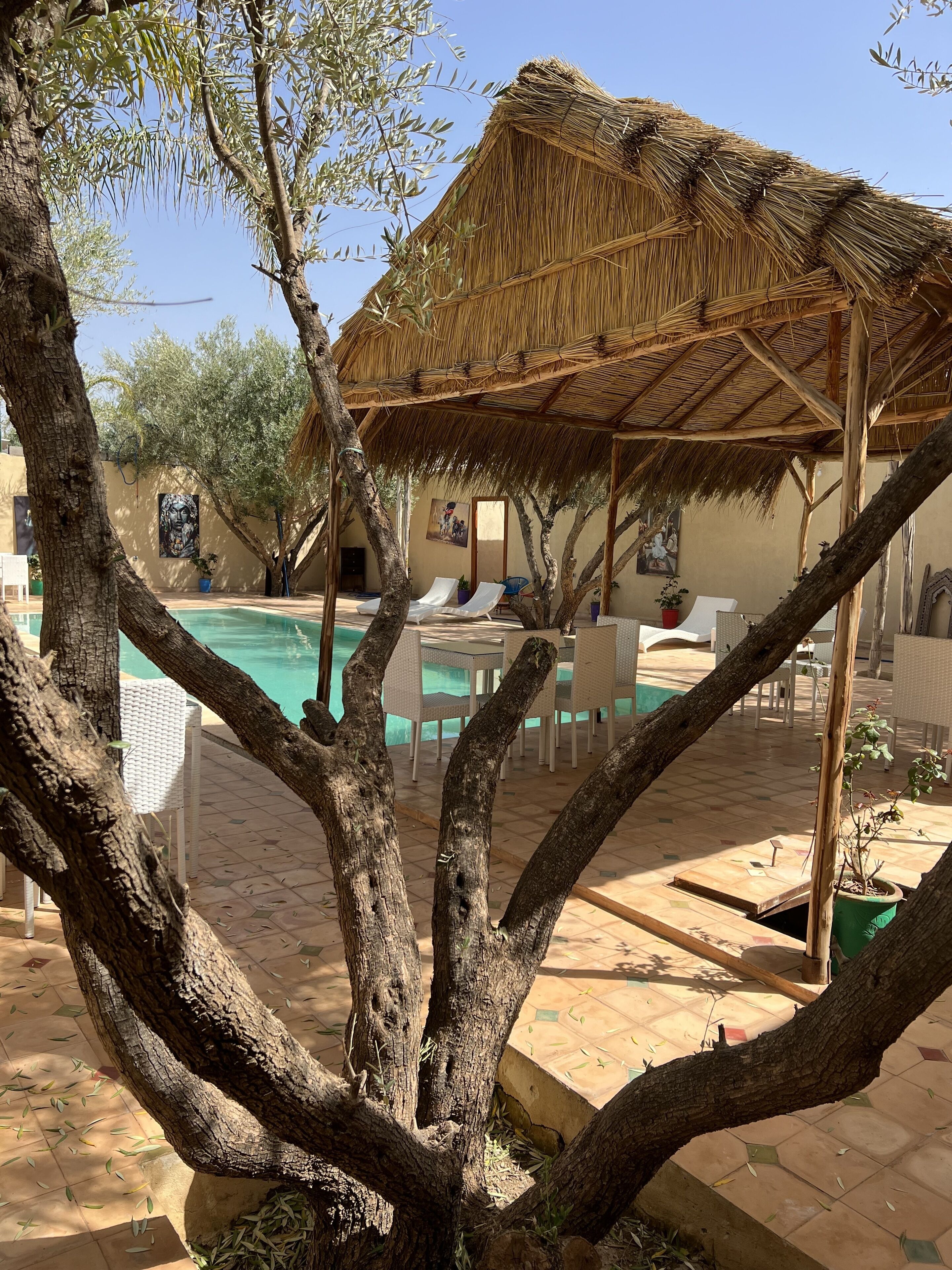 A pool area with a thatched roof structure, lounge chairs, and a tiled floor.