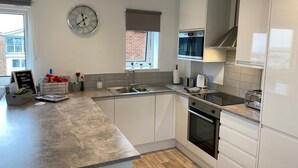 A modern kitchen with white cabinets, a stainless steel sink, and a built-in oven. - Sea-side holiday home with balcony views to the sea (Hunstanton)
