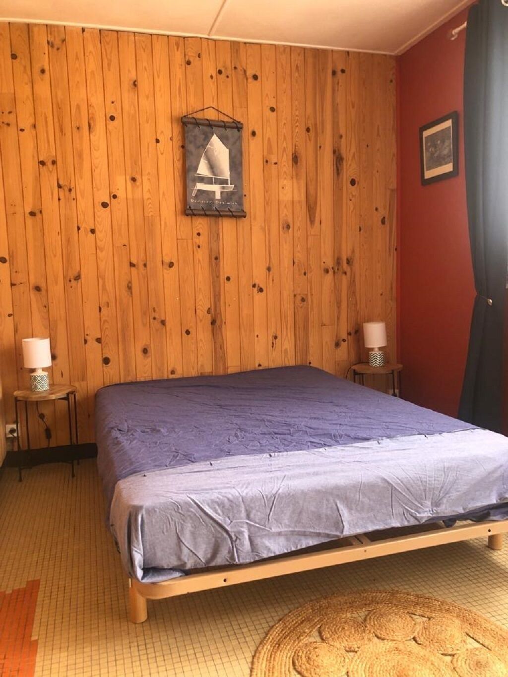 Ein Zimmer mit einer Holzpaneelausstattung, einem Bett mit blauer Bettdecke, zwei Nachttischen mit Lampen und einem Teppich auf dem Boden.