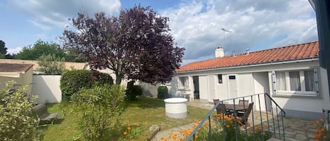 Ett bostadsområde med ett vitt hus, ett träd med lila blad och en trädgård med orange blommor.