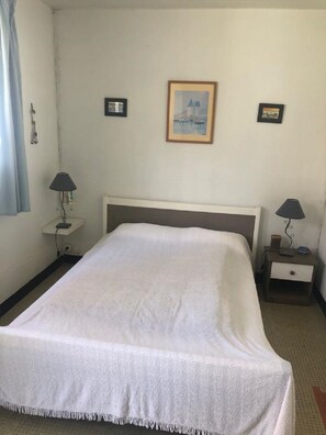 Siististi pedattu sänky hotellihuoneessa, jonka seinä on pelkistetty valkoinen. Sängyn molemmin puolin on yöpöytä, jossa on lamppu, ja seinällä on kaksi kehystettyä kuvaa.