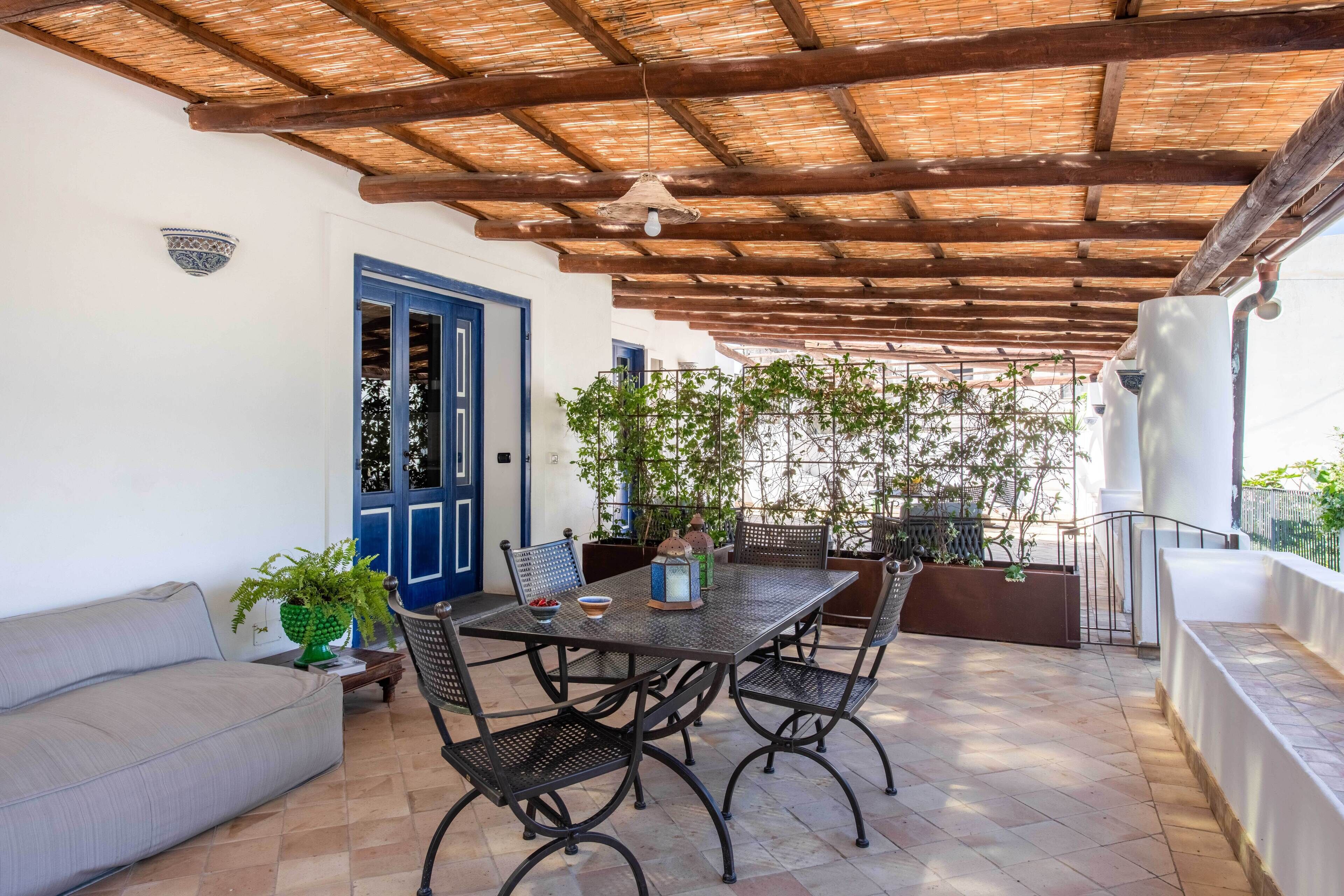 Eine überdachte Terrasse mit Tisch, Stühlen, einer Couch und Kübelpflanzen.
