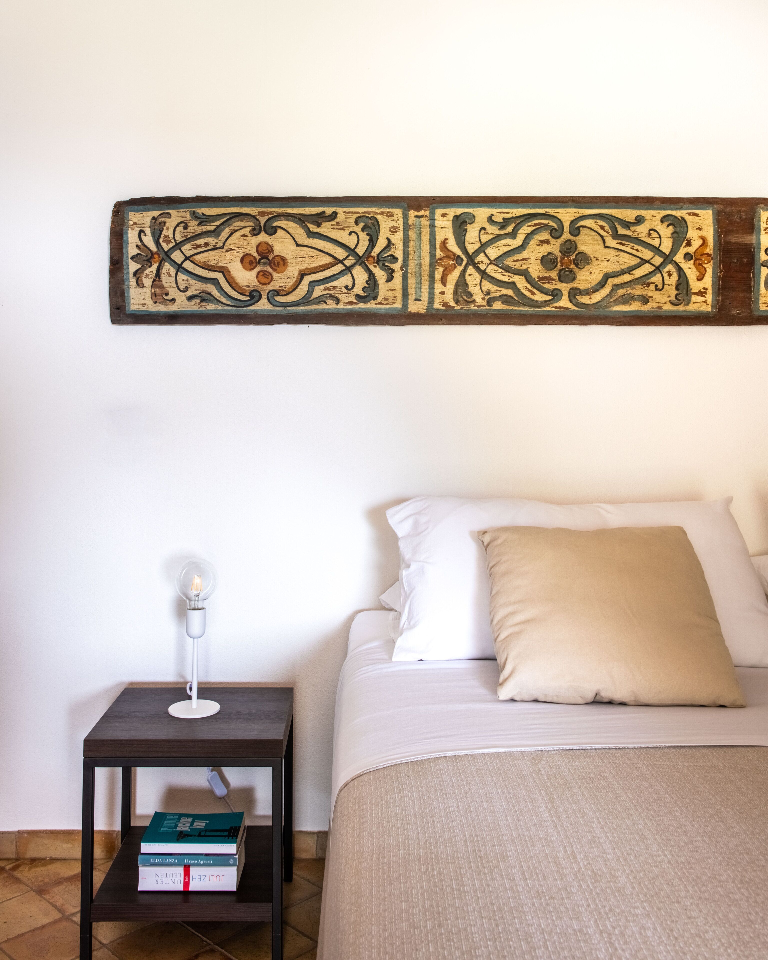A neatly arranged bedroom with a bed, a bedside table with a lamp, and a shelf with books.