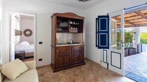 A room with a wooden cabinet, a sofa, a bed, and a view through an open door to an outdoor area with a pergola. - Vico San Lorenzo - Camere a Salina (Malfa)