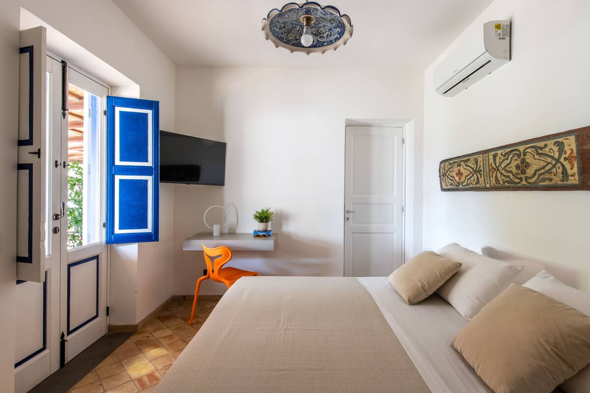Une chambre à coucher avec un lit, un bureau avec une chaise, une télévision et une porte.