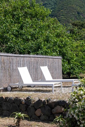 A secluded outdoor seating area with two white lounge chairs and a bamboo wall backdrop, surrounded by lush greenery and a stone wall. - Vico San Lorenzo - Camere a Salina (Malfa)