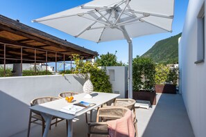 An outdoor patio with a table, chairs, and a large umbrella. - Vico San Lorenzo - Camere a Salina (Malfa)