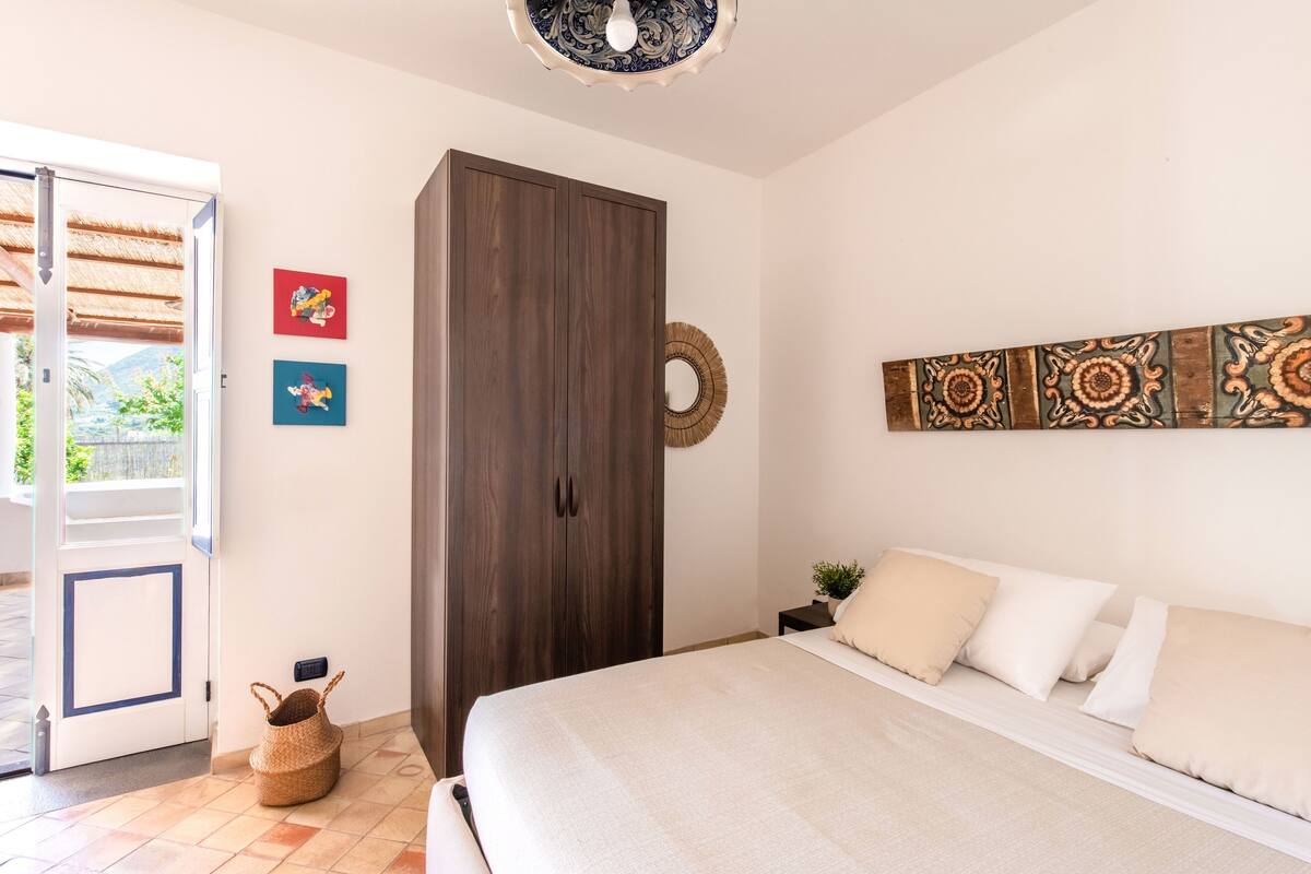 Une chambre à coucher comprenant un lit, une armoire, une porte donnant sur un balcon et des œuvres d’art murales.