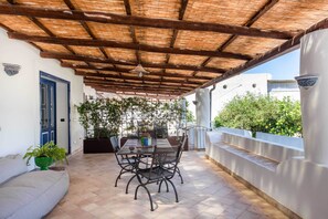 An outdoor patio with a table and chairs, a ceiling with wooden beams, a door, and potted plants. - Vico San Lorenzo - Camere a Salina (Malfa)