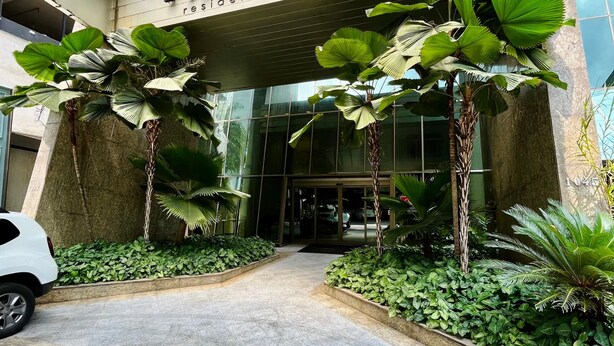 Entrada de um edifício com a inscrição 'PANCETTI' e 'serviço de residência' visíveis. Há plantas em vasos e um caminho pavimentado que leva à entrada.