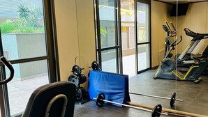 Academia com equipamentos de ginástica, janelas amplas e vista para o exterior.