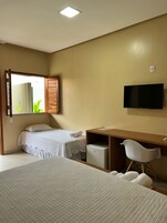 Habitación de hotel con dos camas, un escritorio, una silla, un televisor y un cubo de basura pequeño.