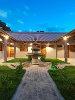 Un patio con una fuente en el centro, rodeado por un corredor cubierto y puertas de madera.