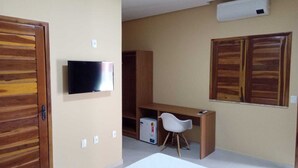 A room with a wooden wardrobe, a television mounted on the wall, a desk with a chair, and a small refrigerator. - Hotel do Carmo (Piracuruca)