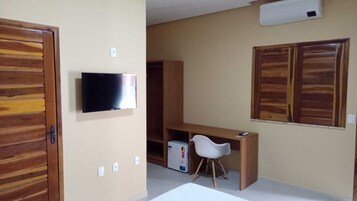 Una habitación con un armario de madera, un televisor montado en la pared, un escritorio con una silla y un refrigerador pequeño.