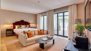 Ein modernes Hotelzimmer mit einem großen Bett, einer Couch, einem Couchtisch und Blick ins Freie durch große Fenster.