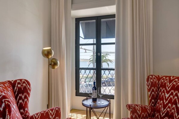A room with two red patterned sofas, a small round table with a bottle and glass, and a floor lamp.