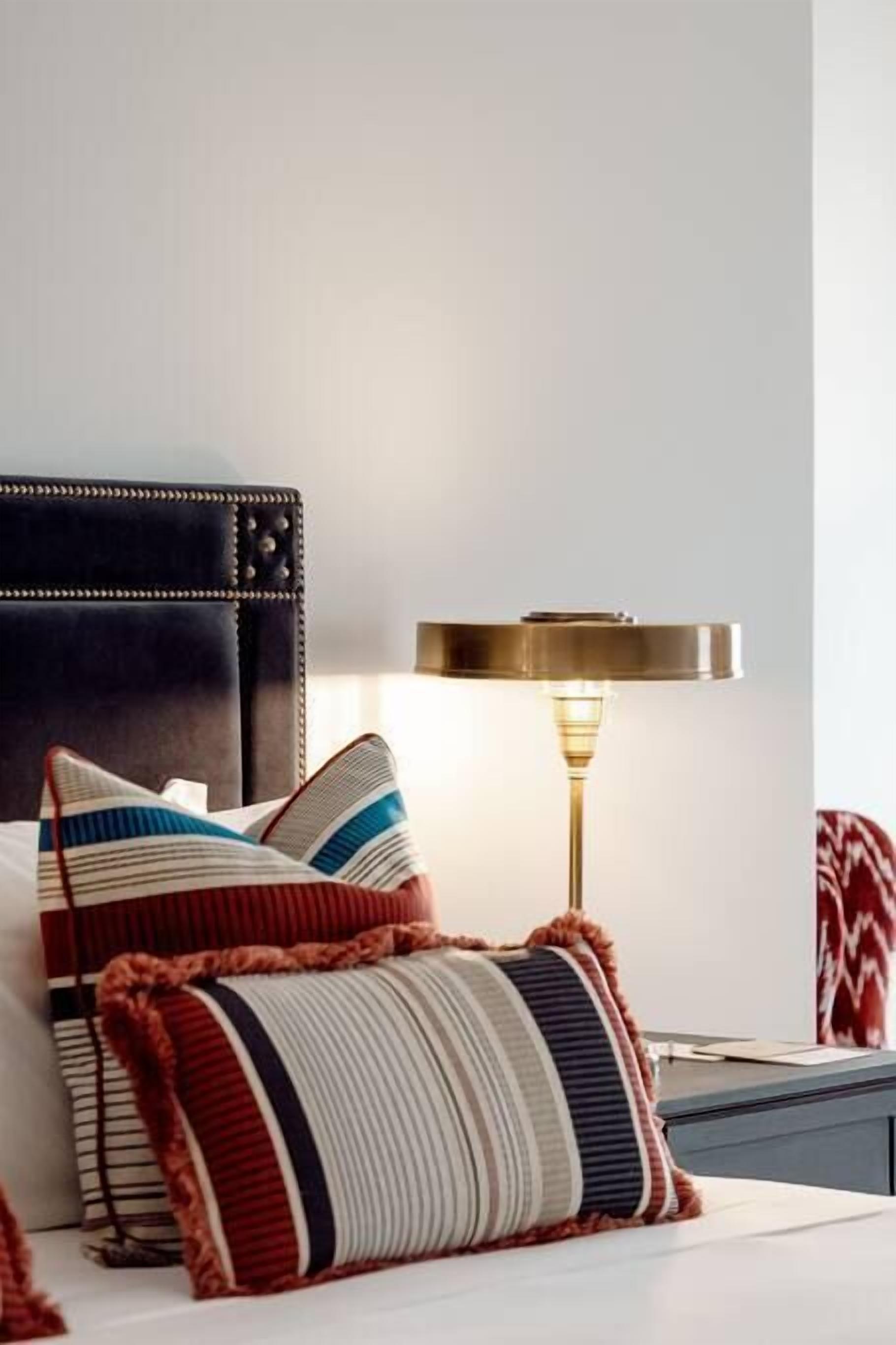 A bed with striped pillows and a gold table lamp.