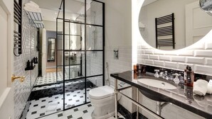 Une salle de bain moderne avec une douche à l’italienne en verre, des toilettes blanches, un lavabo noir et un grand miroir.