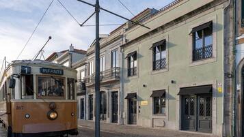 A vintage tram labeled "INFANTE" with the number 287, traveling on tracks alongside historic buildings with balconies and traditional architecture.