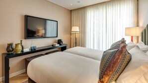 Une chambre d’hôtel avec deux lits, un téléviseur à écran plat, un bureau avec une lampe et une grande fenêtre avec des rideaux.
