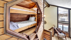 A cabin with a loft-style sleeping area, a small seating area with a bench and chair, and a window offering a view of the outdoors. - Snowshoe Village 5A Ski In/Out Condo (Brian Head)