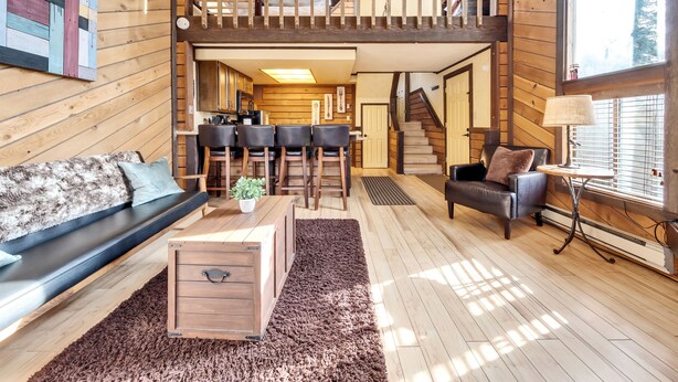 A spacious loft-style living area with a wooden floor, a loft bed, a sofa, a coffee table, and a dining table with chairs. - Snowshoe Village 5A Ski In/Out Condo (Brian Head)