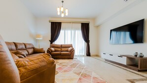A modern living room with a brown leather sofa, a matching armchair, a patterned rug, a flat-screen TV, and a wooden side table. - Luxury doublex apartments in new cairo
شقق فندقيه للايجار بالتجمع الخامس  (Cairo)