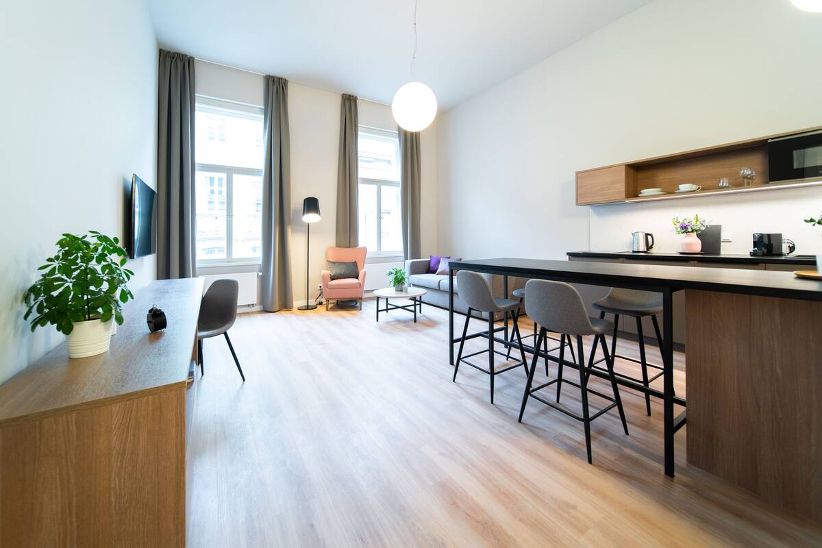A modern kitchen with a wooden countertop, bar stools, and a large window with curtains.